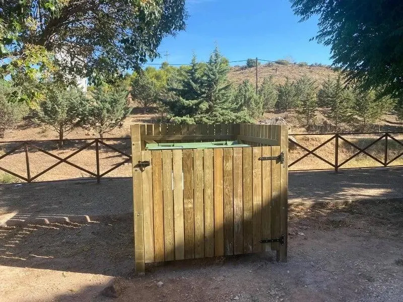 Cubrecontenedor de madera sin tejado para un contenedor, junto a una valla de madera en el campo