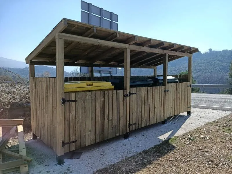 Cubrecontenedor de madera para tres contenedores con tejado, junto a una carretera de montaña