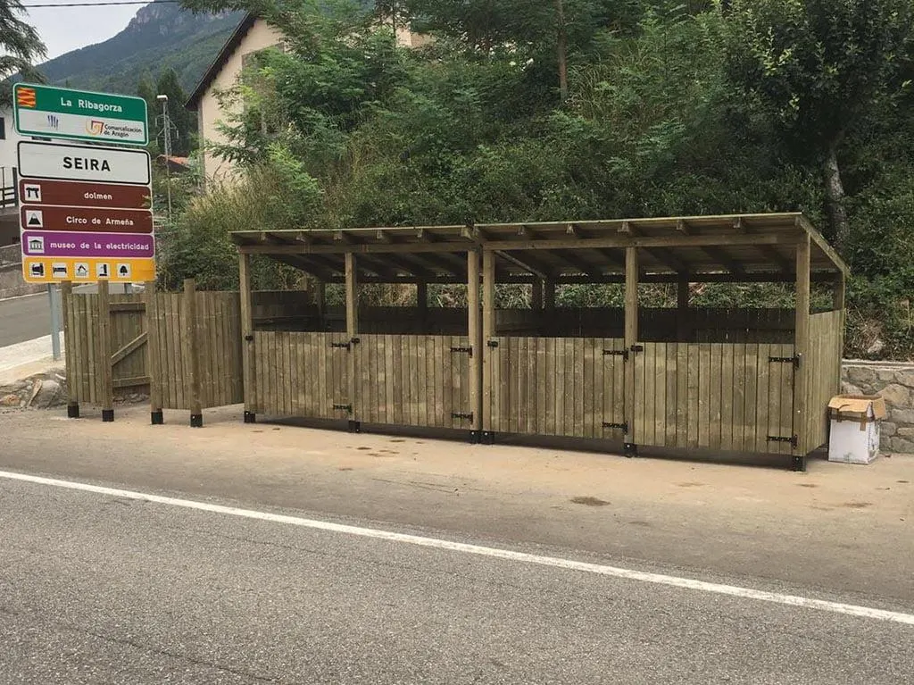 Cubrecontenedor de madera a medida con tejado para varios contenedores, junto a una carretera