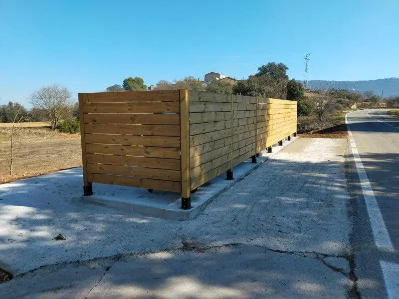 Cubrecontenedor de madera de tablas horizontales a lo largo de una carretera