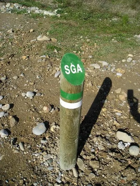 Baliza de madera con chapa verde de sendero local clavada en el terreno