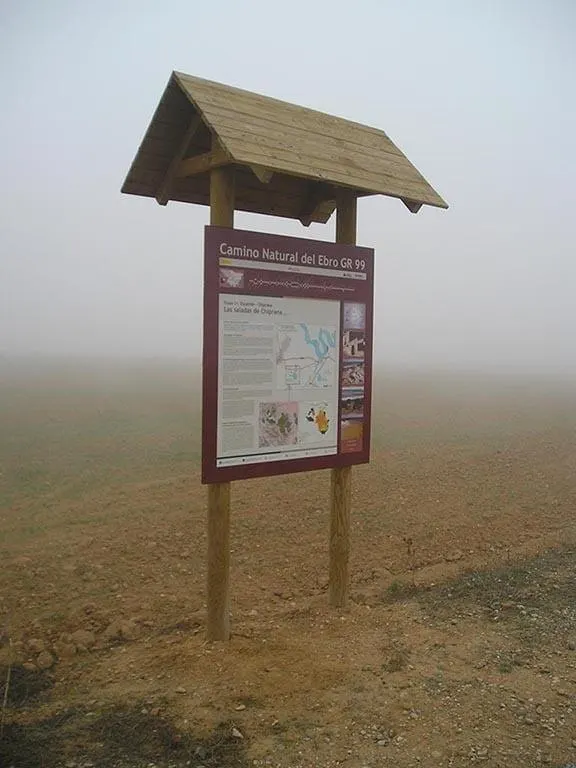 Cartel de madera modelo CN-01 con tejadillo a dos aguas y pilares de rollizo junto a un camino