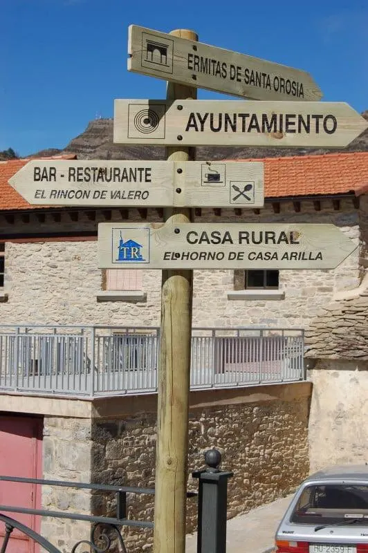 Poste de madera con flechas de dirección grabadas hacia el ayuntamiento, un restaurante y una casa rural