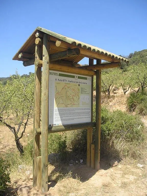 Cartel de madera modelo Somontano con tejadillo de medios rollizos entre almendros